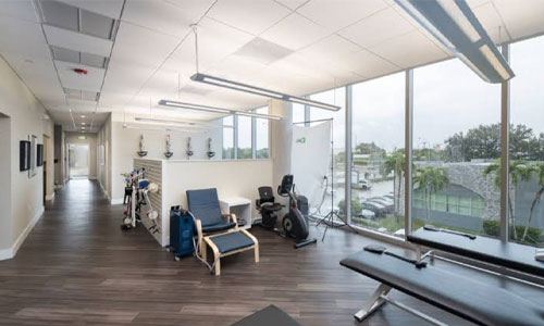 Open rehabilitation area with treatment tables, exercise equipment and waterfront view